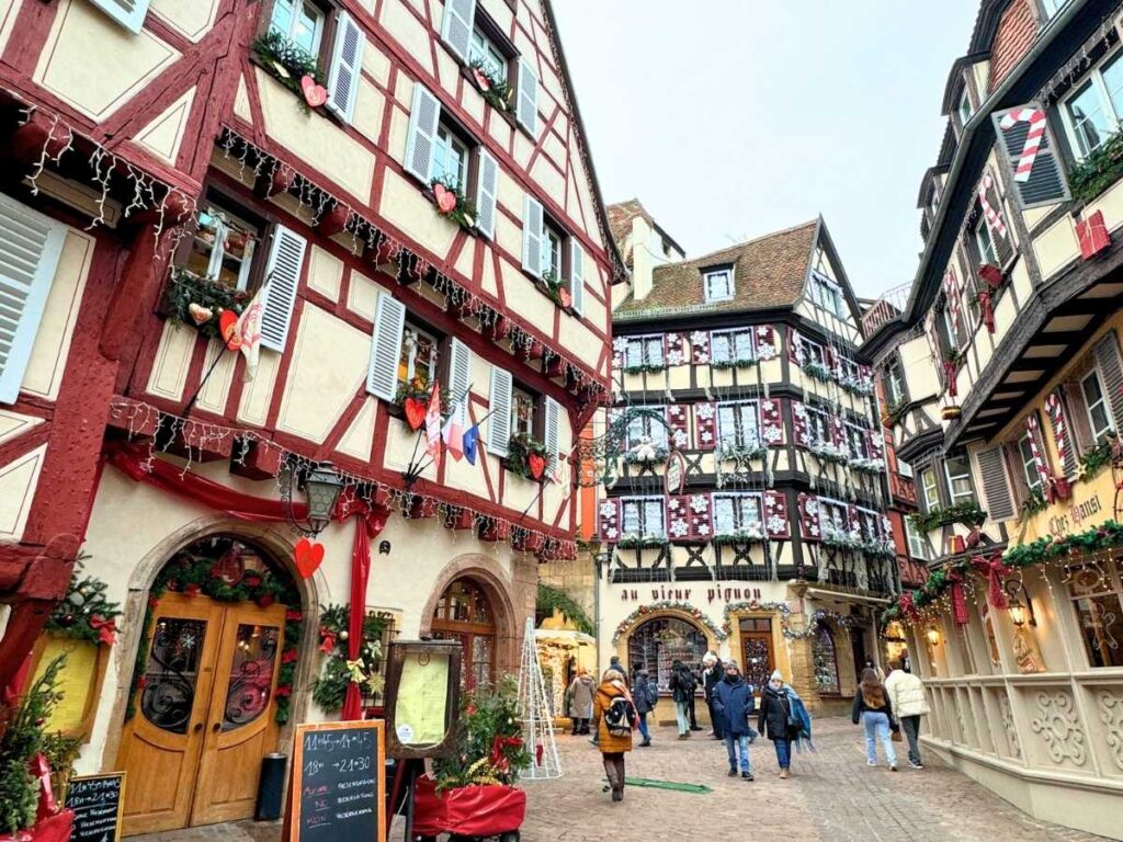 Half-timbered houses in Colmar are beautifully decorated with hearts and Christmas ornaments as visitors stroll the street.