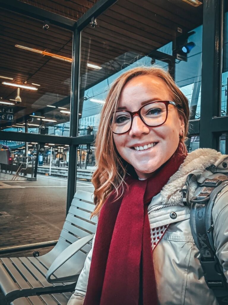 Kate takes a cheerful selfie while waiting at a train station.