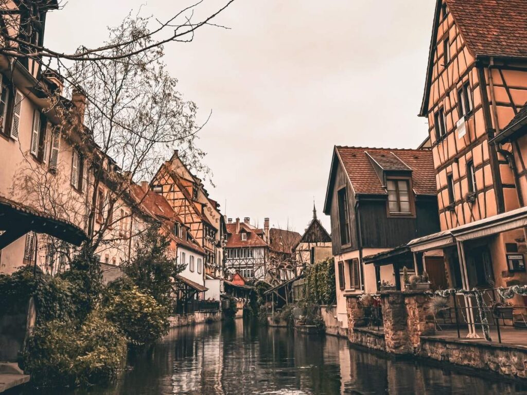 A peaceful canal in Colmar is lined with half-timbered houses and winter trees.