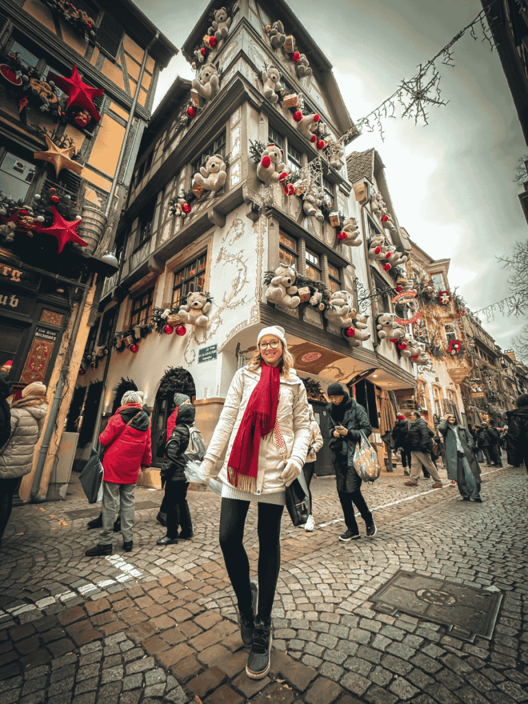 Kate smiles in front of a Strasbourg building decorated with teddy bears and festive ornaments during Christmas.