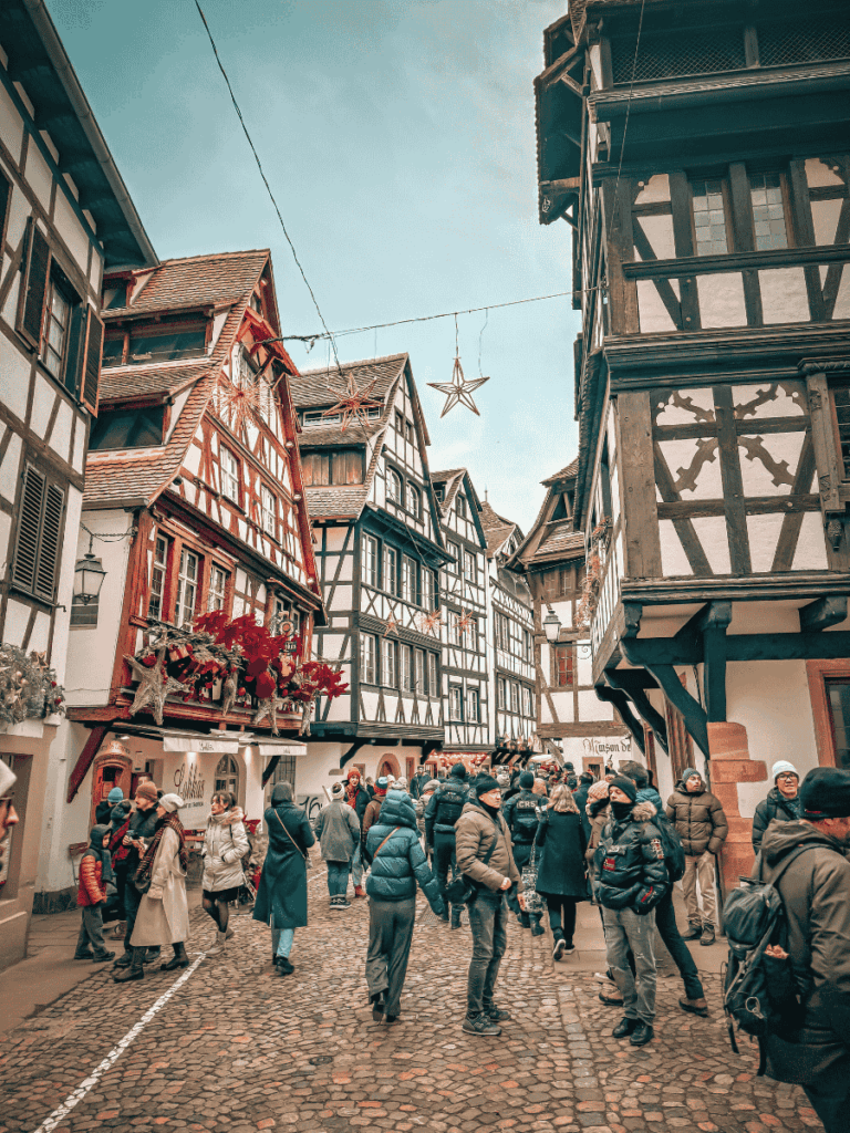 Crowds walk through Strasbourg’s Petite France, surrounded by half-timbered houses decorated for Christmas.