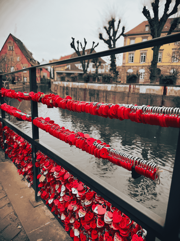 A bridge in Colmar is covered with red heart-shaped love locks overlooking the canal.