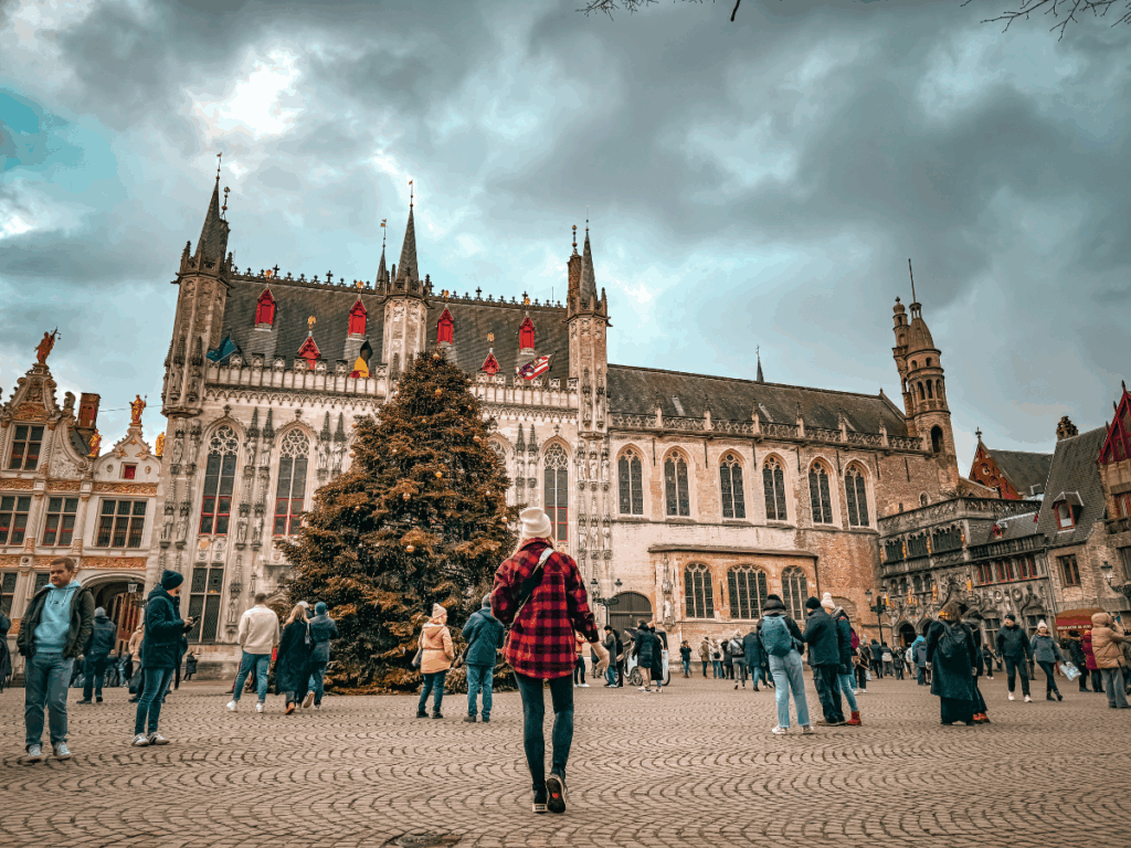 Kate walks across Bruges’ main square toward a towering Christmas tree in front of the Gothic City Hall.