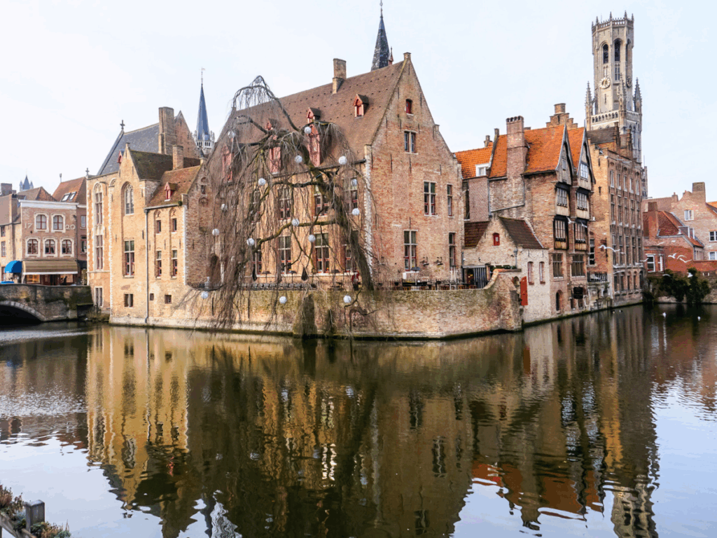Historic brick buildings and the Belfry of Bruges are reflected in the still canal waters at the city’s famous Rozenhoedkaai viewpoint.