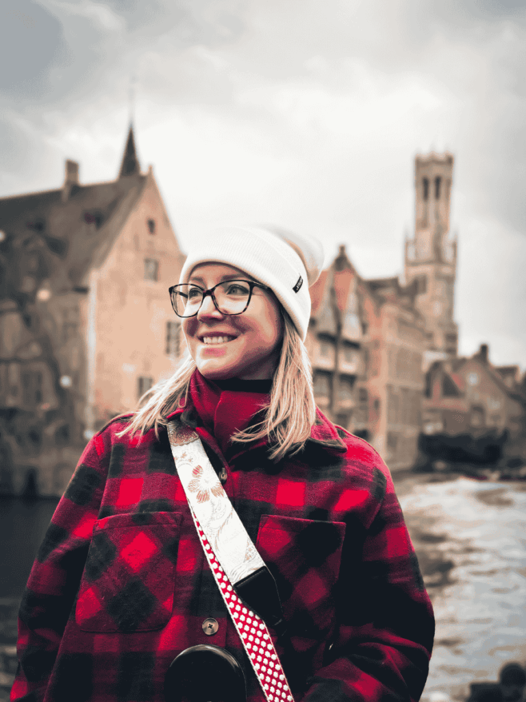 Kate smiles in front of the canal houses of Bruges with the Belfry tower in the background.