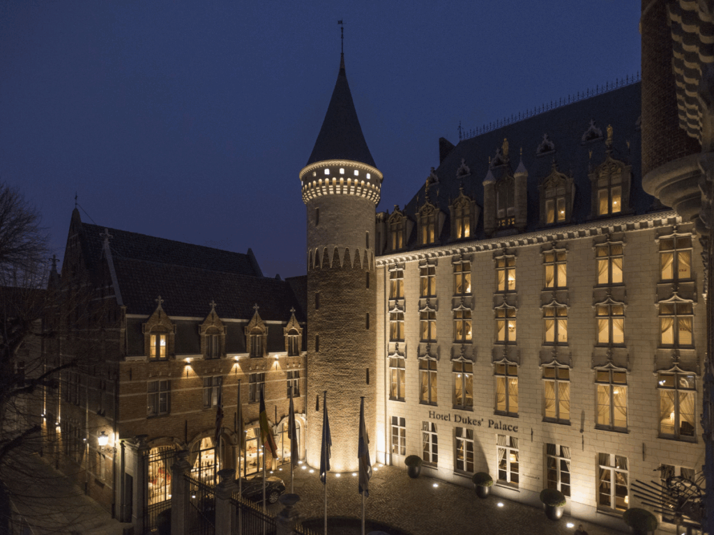 The Hotel Dukes’ Palace in Bruges glows warmly at night with its lit windows and castle-like tower.