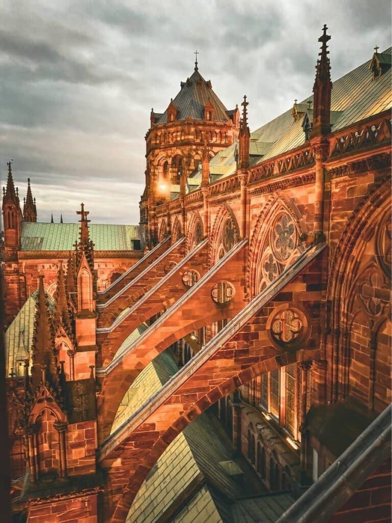 A close-up of Strasbourg Cathedral’s upper façade shows its intricate stonework and flying buttresses under a moody sky.