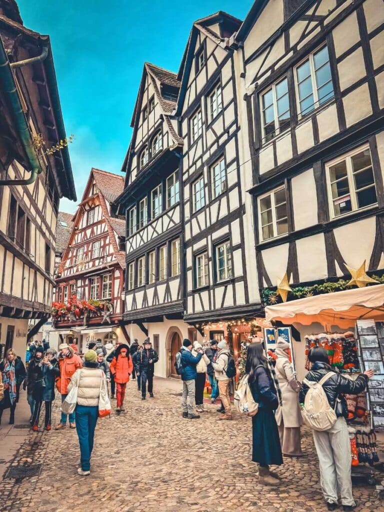 Tourists stroll through Strasbourg’s Petite France, lined with charming half-timbered houses and festive holiday stalls.