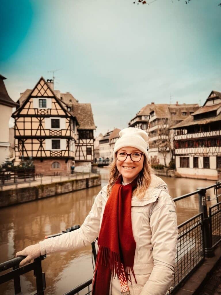 Kate smiles by the river in Strasbourg’s Petite France, framed by traditional Alsatian buildings.