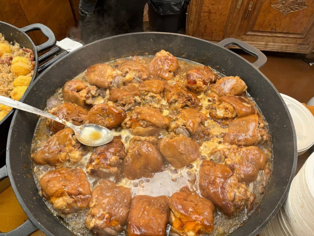 A large pan of braised pork knuckles simmers in a rich, savory sauce at a Strasbourg Christmas market food stall.