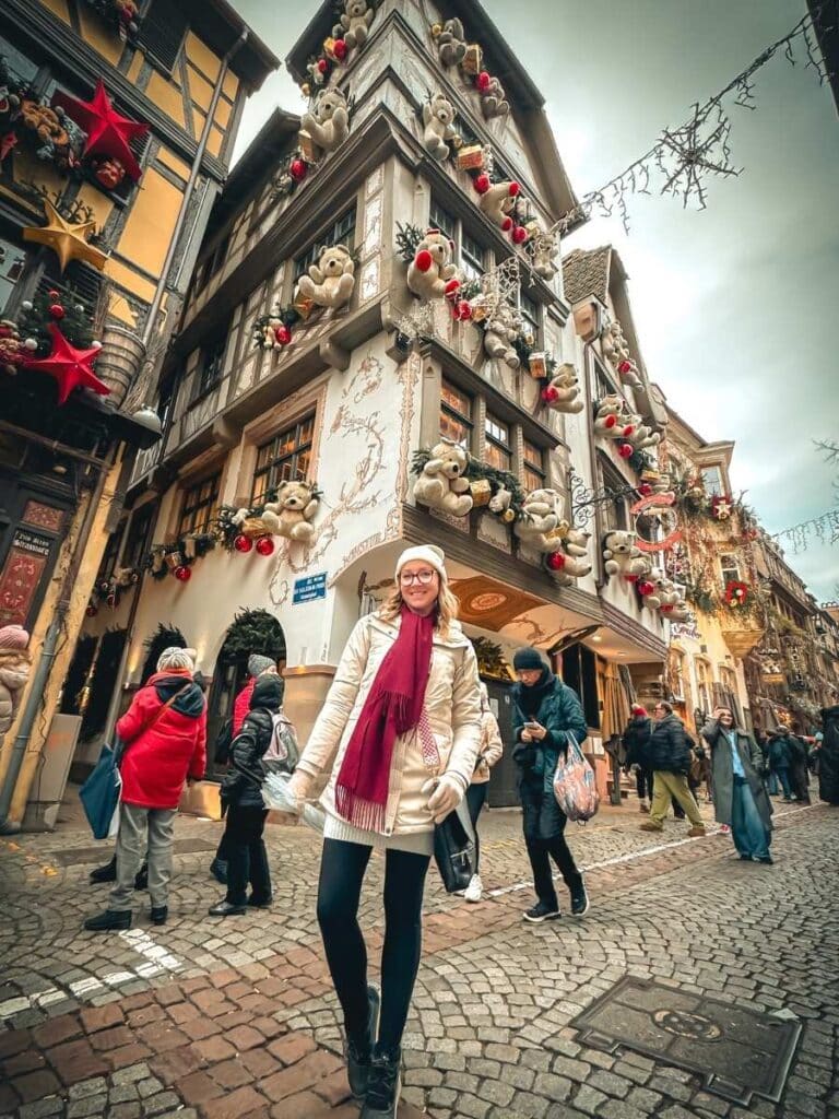 Kate poses on a cobblestone street in front of a Strasbourg building lavishly decorated with Christmas bears and ornaments.