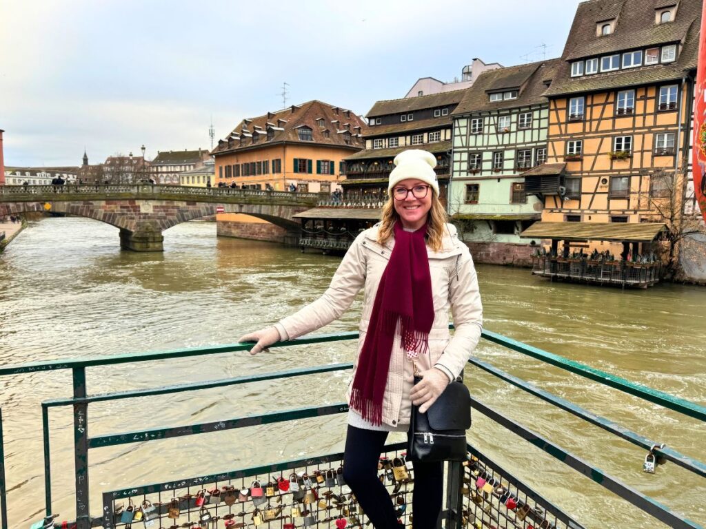 Kate poses on a bridge in Strasbourg with the river and colorful timbered houses in the background.