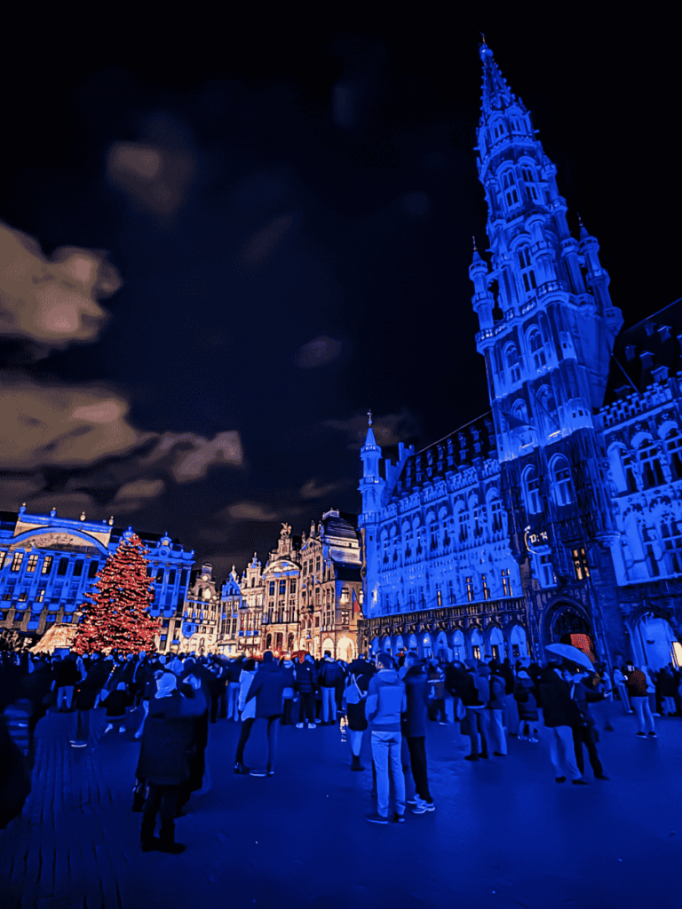 Brussels’ Grand Place glows blue at night with a towering Christmas tree and festive crowds.