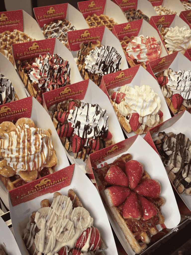 A display of colorful Belgian waffles is topped with strawberries, cream, and drizzled sauces.