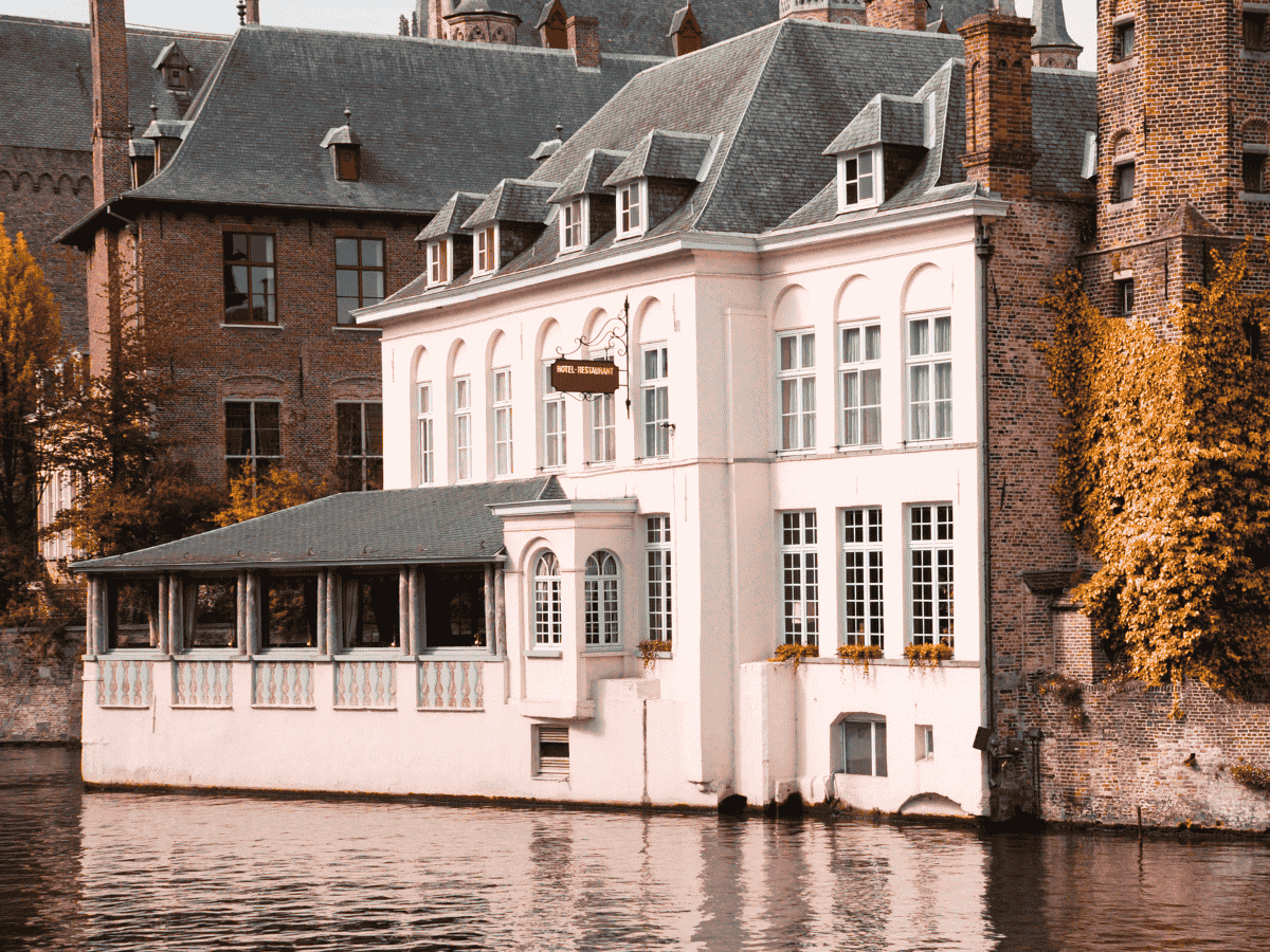 A charming white canal-side hotel and restaurant in Bruges reflects softly in the calm water.