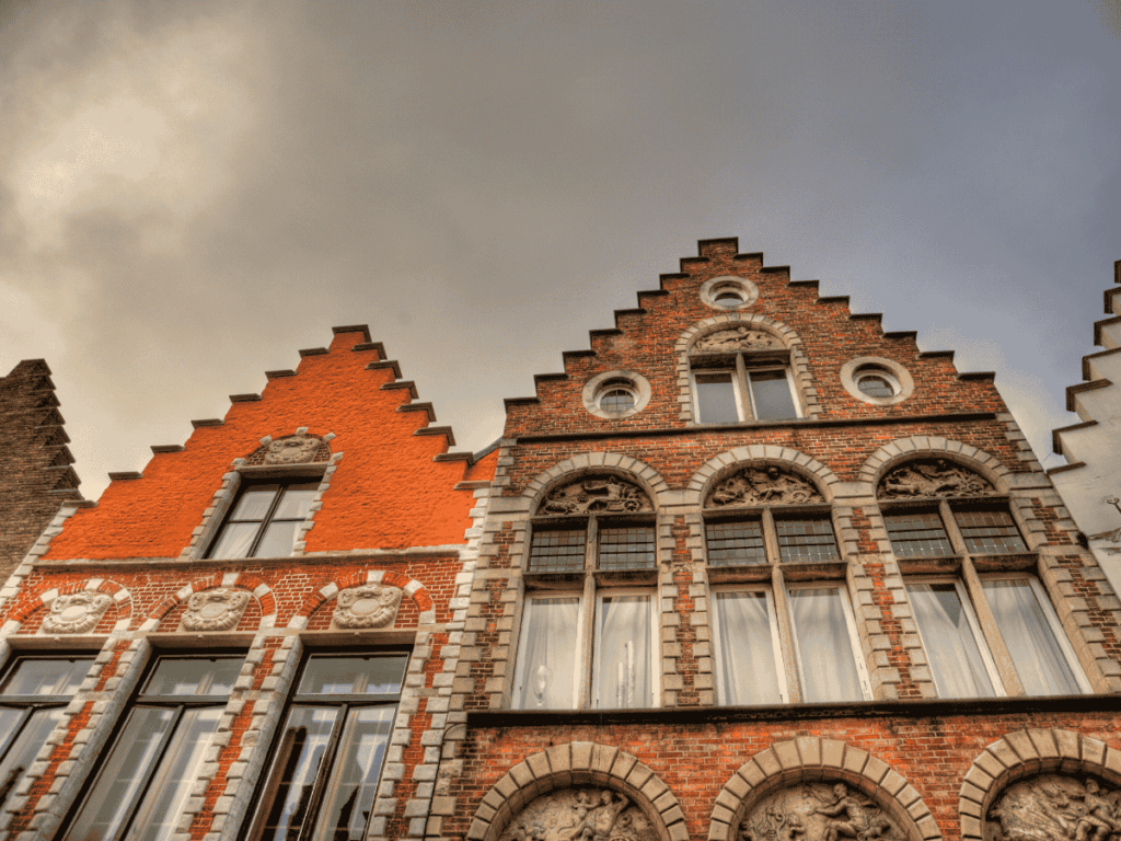 Ornate stepped-gable brick buildings in Bruges glow warmly under a cloudy evening sky.