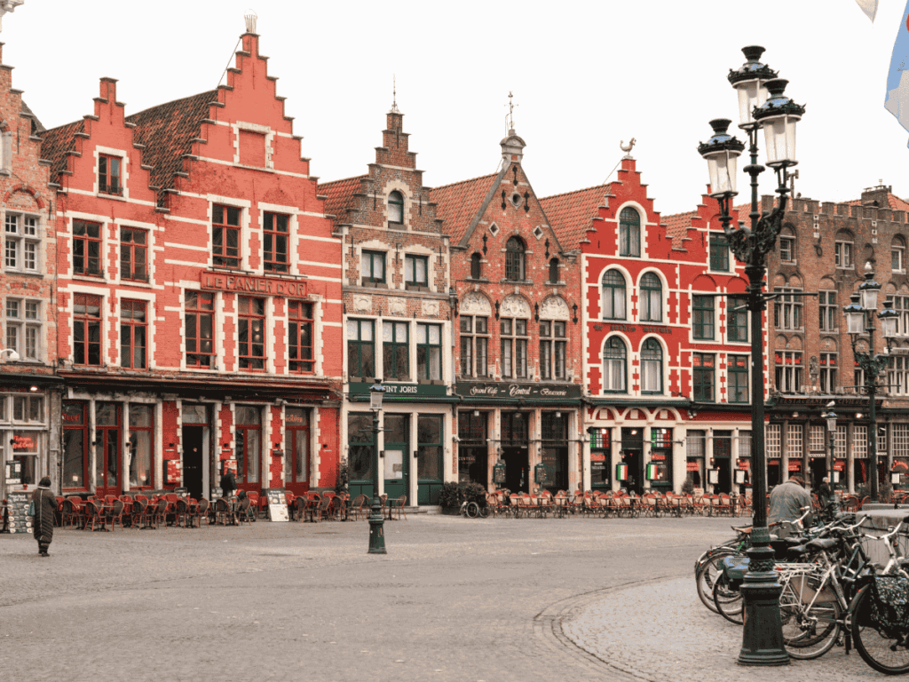Colorful stepped-gable buildings line the Markt square in Bruges, with rows of café tables and bicycles in the foreground.
