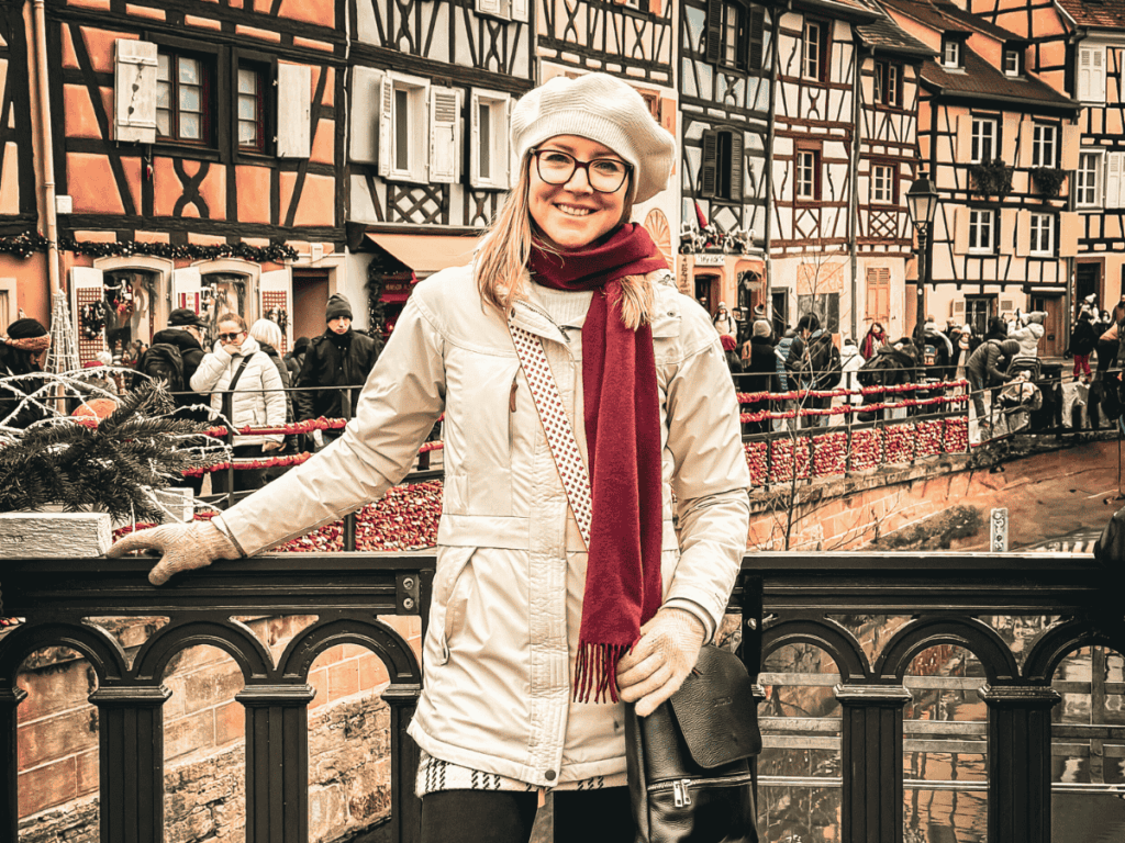 Kate poses on a bridge over the canal in Colmar’s Little Venice, surrounded by half-timbered houses and holiday decorations.