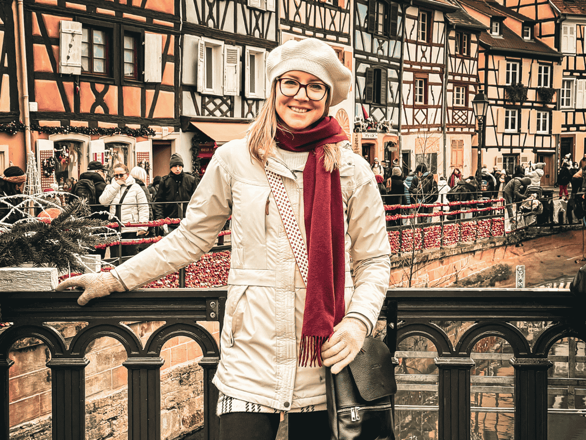 Kate poses on a bridge over the canal in Colmar’s Little Venice, surrounded by half-timbered houses and holiday decorations.