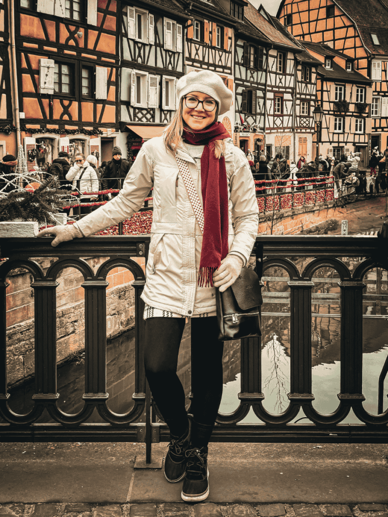 Kate poses on a bridge over the canal in Colmar’s Little Venice, surrounded by half-timbered houses and holiday decorations.