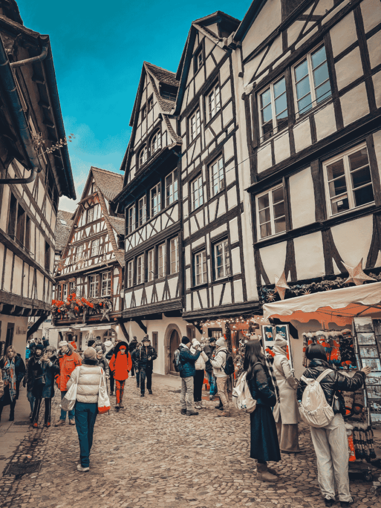 People stroll through a cobblestone street in Strasbourg’s Petite France, surrounded by half-timbered houses and festive market stalls.