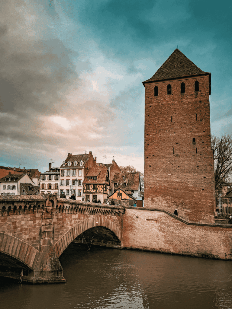 A medieval brick tower rises beside a stone bridge over the river in Strasbourg’s historic district.