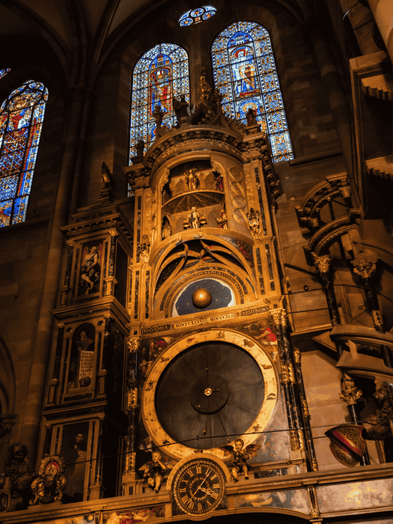 The ornate astronomical clock inside Strasbourg Cathedral glows warmly beneath intricate stained-glass windows.