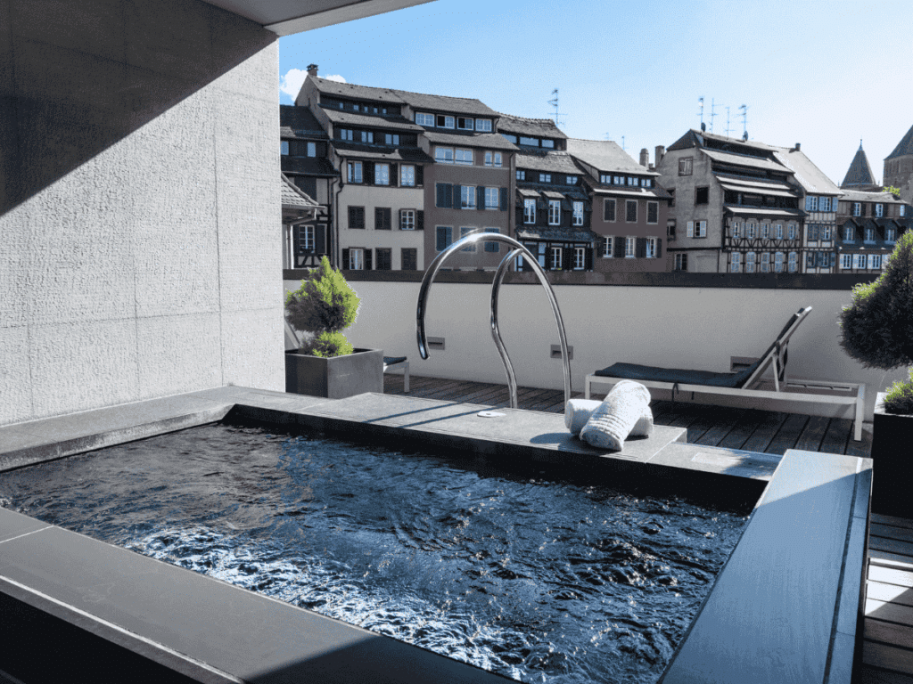 Private spa pool on a rooftop deck at Hôtel & Spa Régent Petite France with lounge chairs, rolled towels, and a view of Strasbourg’s charming old town architecture.
