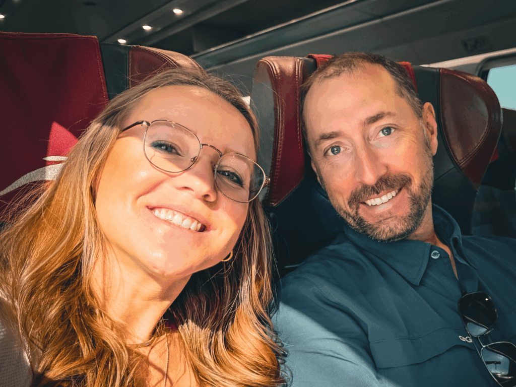 Kate and her travel companion smile in a close-up selfie while seated together on a European train.
