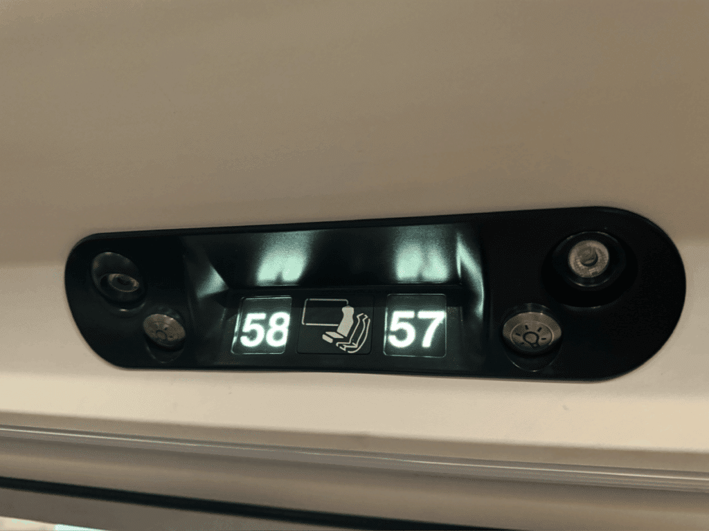 Close-up of illuminated seat numbers 57 and 58 on a European train, with icons indicating a table and legroom in the seating area.