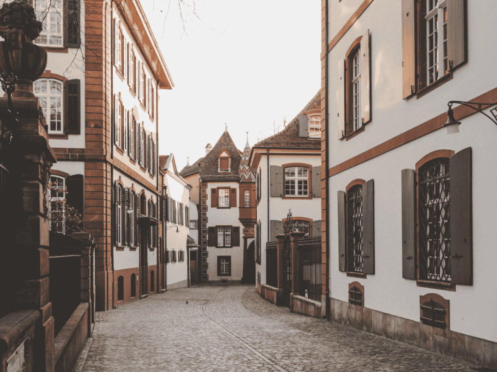 A quiet cobblestone street in Basel’s Old Town is lined with charming shuttered buildings in warm evening light.