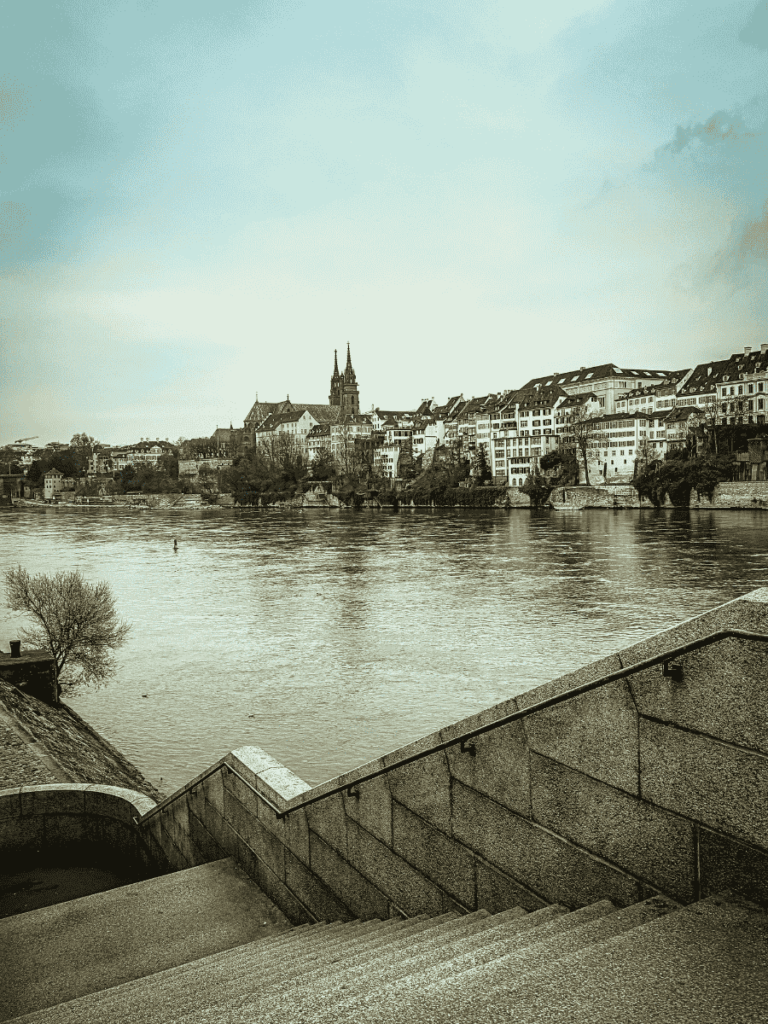 Stone steps descend toward the Rhine River in Basel, offering a wide view of the city’s historic skyline and the twin spires of Basel Minster.
