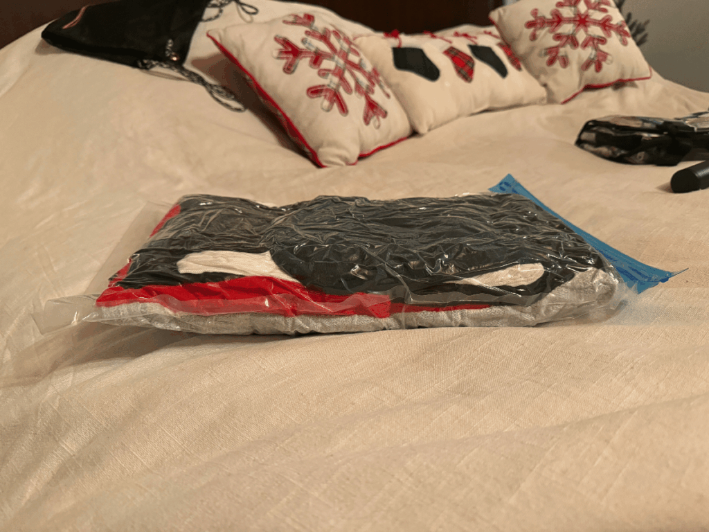 A flatter version of the same packed compression bag filled with winter clothing, showing how space is saved after air is removed, resting on a neatly made bed.