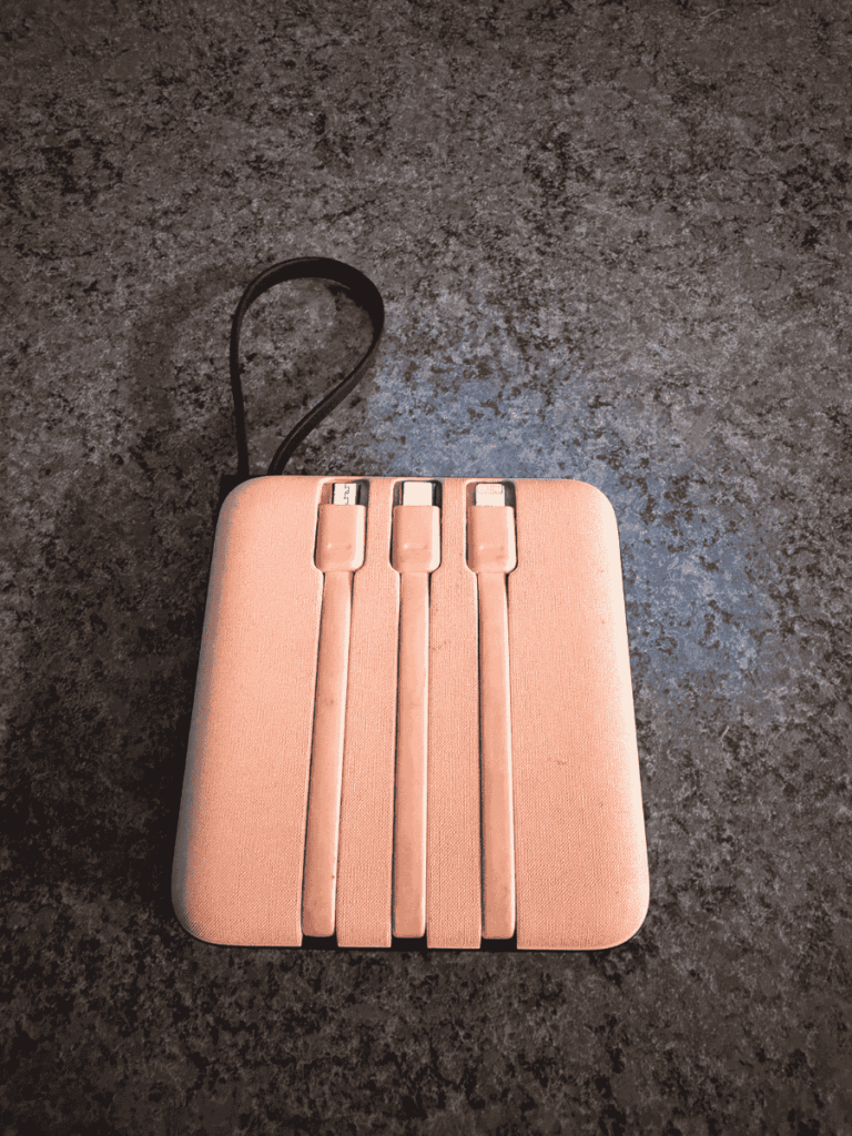 Back of the same power bank case revealing built-in charging cables for USB-C, micro-USB, and Lightning neatly stored in grooves.