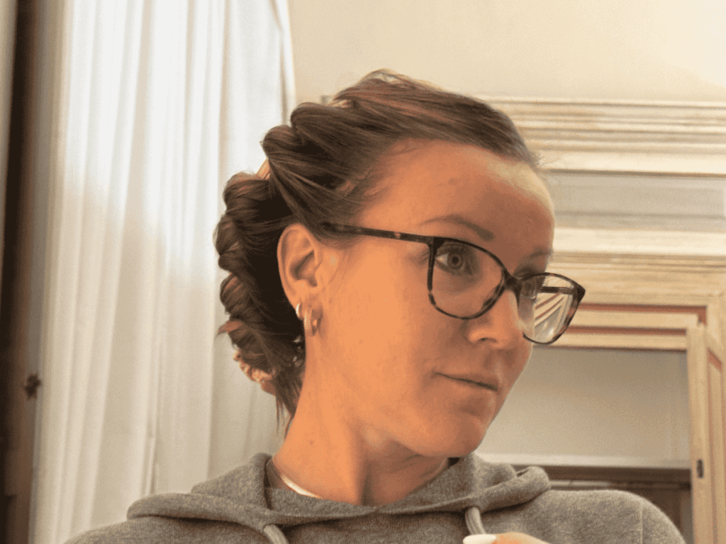 Close-up of a Kate wearing glasses and a hoodie with a heatless robe curler wrapped through her hair in soft twists, creating curls without heat.