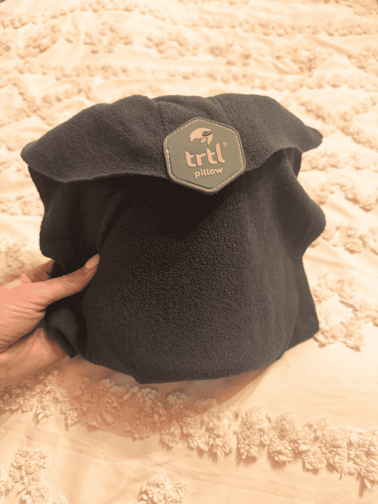 Soft black Trtl travel pillow shown wrapped up and compact, with its logo patch displayed prominently on the front.
