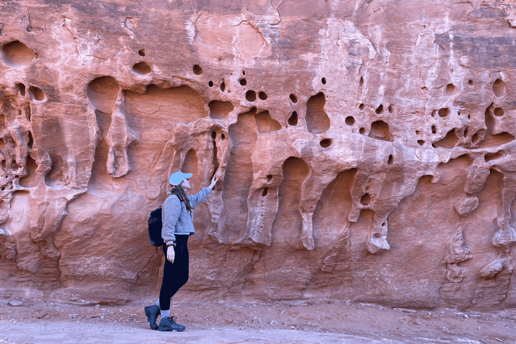 Kate reaches out to touch a textured red rock wall dotted with small, weathered holes and formations in Arches National Park.