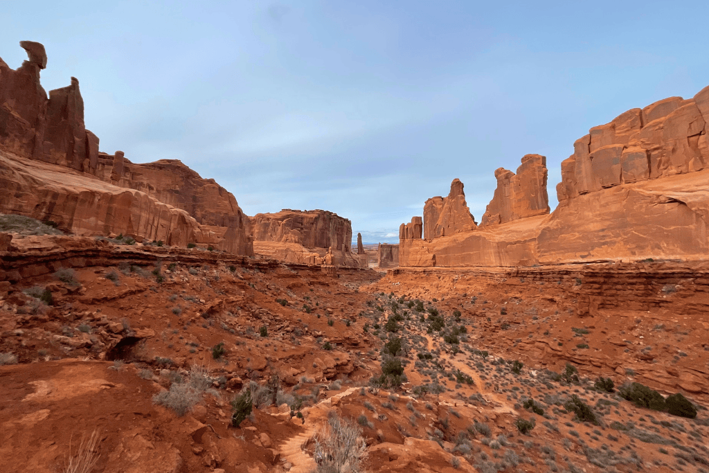 Expansive view of Park Avenue in Arches National Park, with towering red sandstone walls lining a rugged desert valley under a soft, overcast sky.