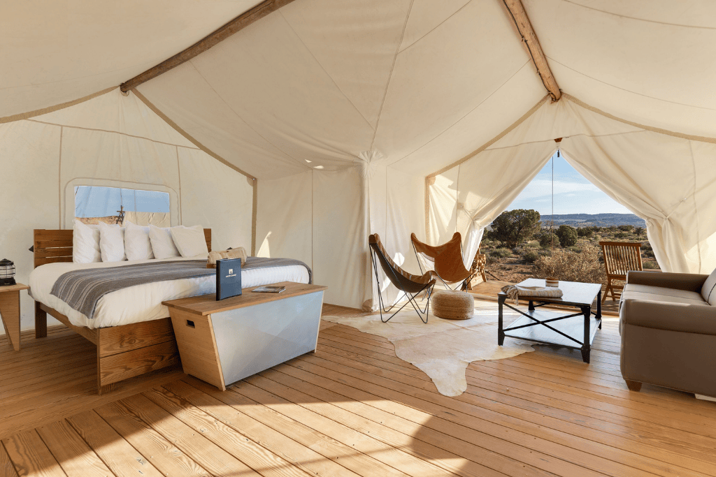 Spacious luxury glamping tent with a king-size bed, leather butterfly chairs, a sofa, and a private deck overlooking desert landscape near Arches National Park.