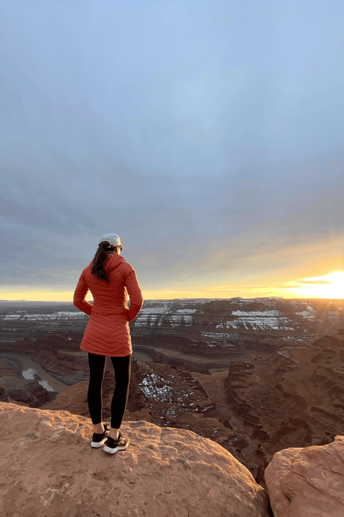 Kate stands at the edge of Dead Horse Point, looking out over the winding Colorado River and snow-dusted canyons as the sun rises on the horizon.