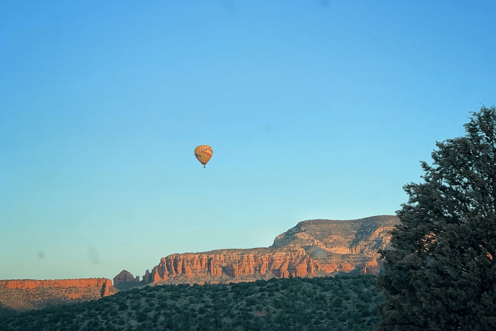 Yellow hot air balloon drifts in a blue sky over Sedona's desert landscape.