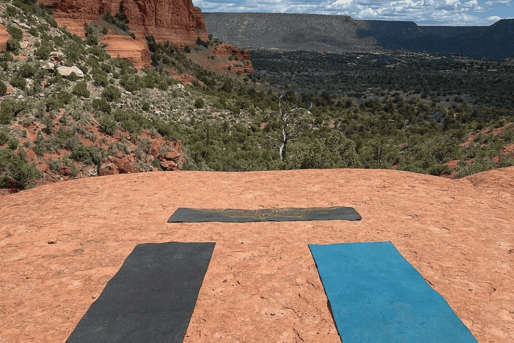 three yoga mats spread out on a flat red rock surface with views of Sedona.