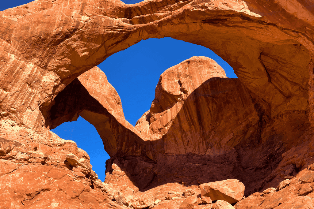 A dramatic view looking up at the intersecting stone spans of Double Arch set against a deep blue sky.