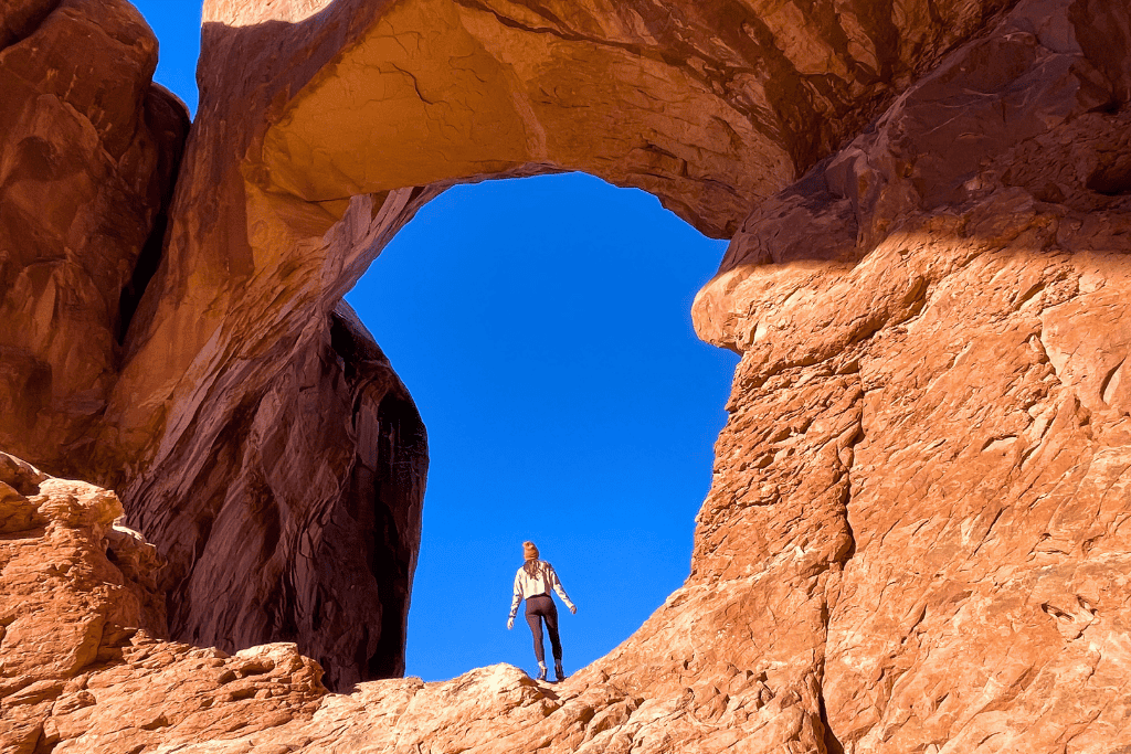 Kate stands beneath one of the soaring arches of Double Arch, framed by towering red rock and clear desert skies.

You said:
She Knows Alt Text said:

A sweeping desert landscape dotted with red rock formations is framed by the curve of a sandstone arch under a brilliant blue sky in Arches National Park.