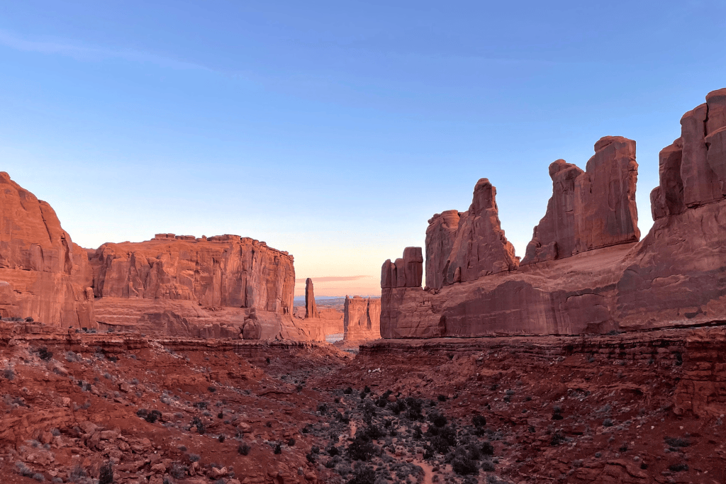 Towering sandstone cliffs glow in the soft light of sunset, lining a dramatic canyon in the Park Avenue section of Arches National Park.