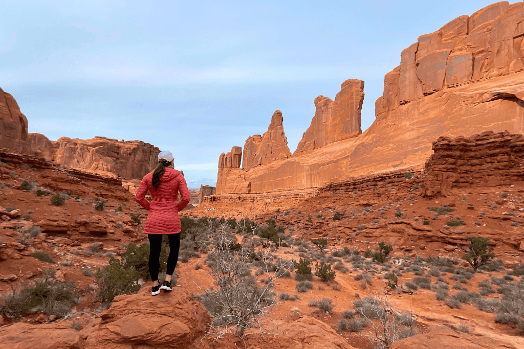 Kate stands on a rock overlooking the towering formations of Park Avenue in Arches National Park, taking in the vast desert canyon.