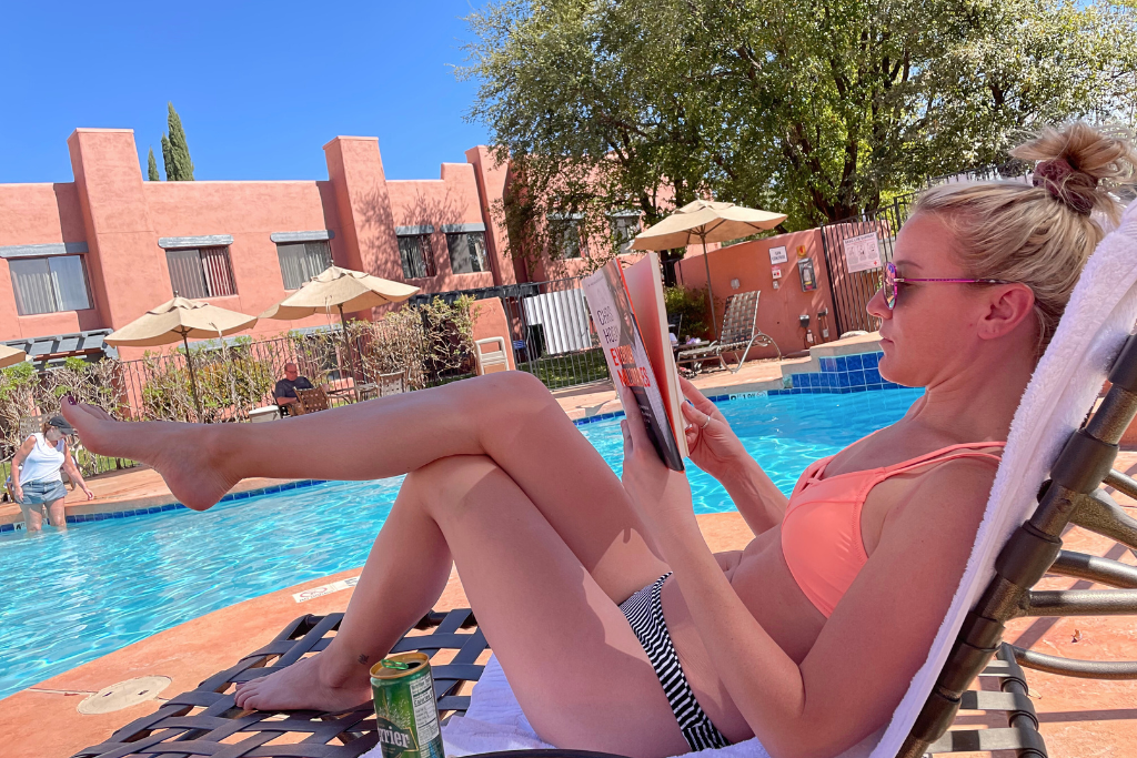 Kate relaxing by her hotel pool reading a book in the sunshine.