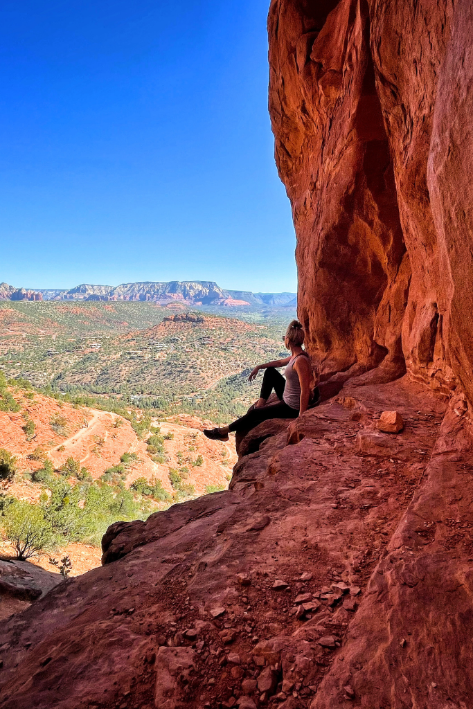 Kate sits on a red rock cliff ledge with legs dangling over.
