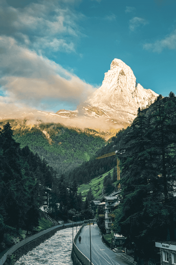 The Matterhorn glows in golden light above a winding river and road leading through the village of Zermatt, Switzerland.