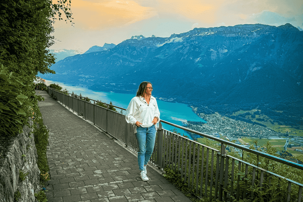 Kate strolls a mountainside path overlooking the vibrant turquoise waters of Lake Brienz and the town of Interlaken nestled in the Swiss Alps.